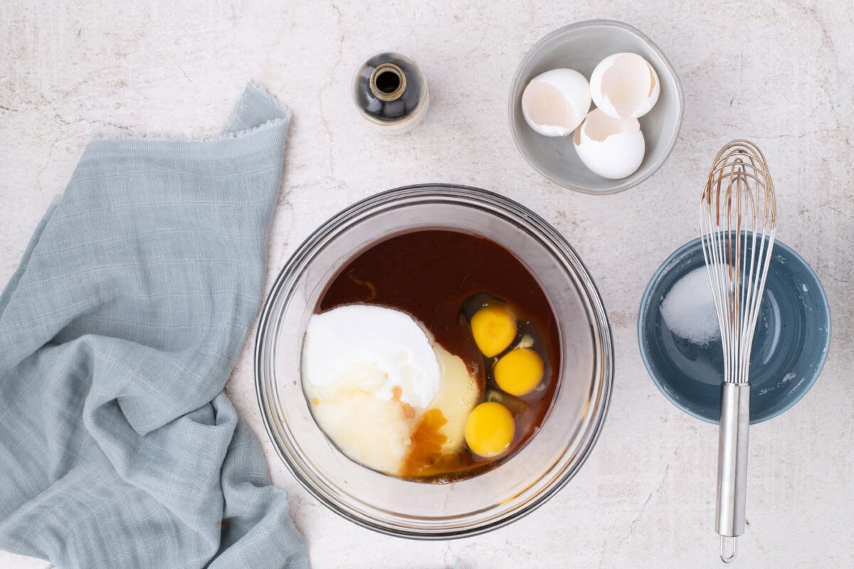 adding eggs and sugar to melted chocolate in a bowl