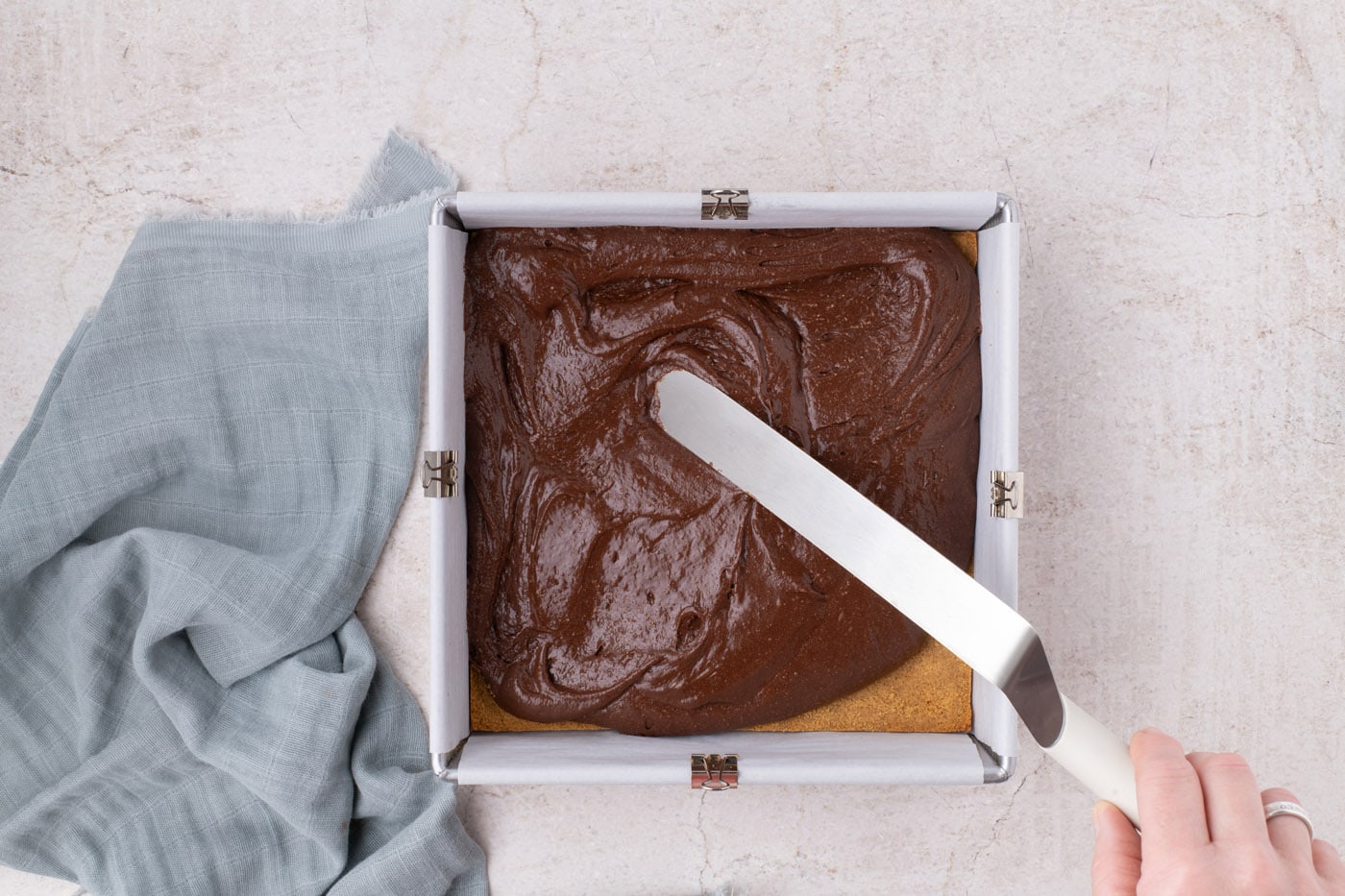 spreading brownie batter over graham cracker crust in a baking pan