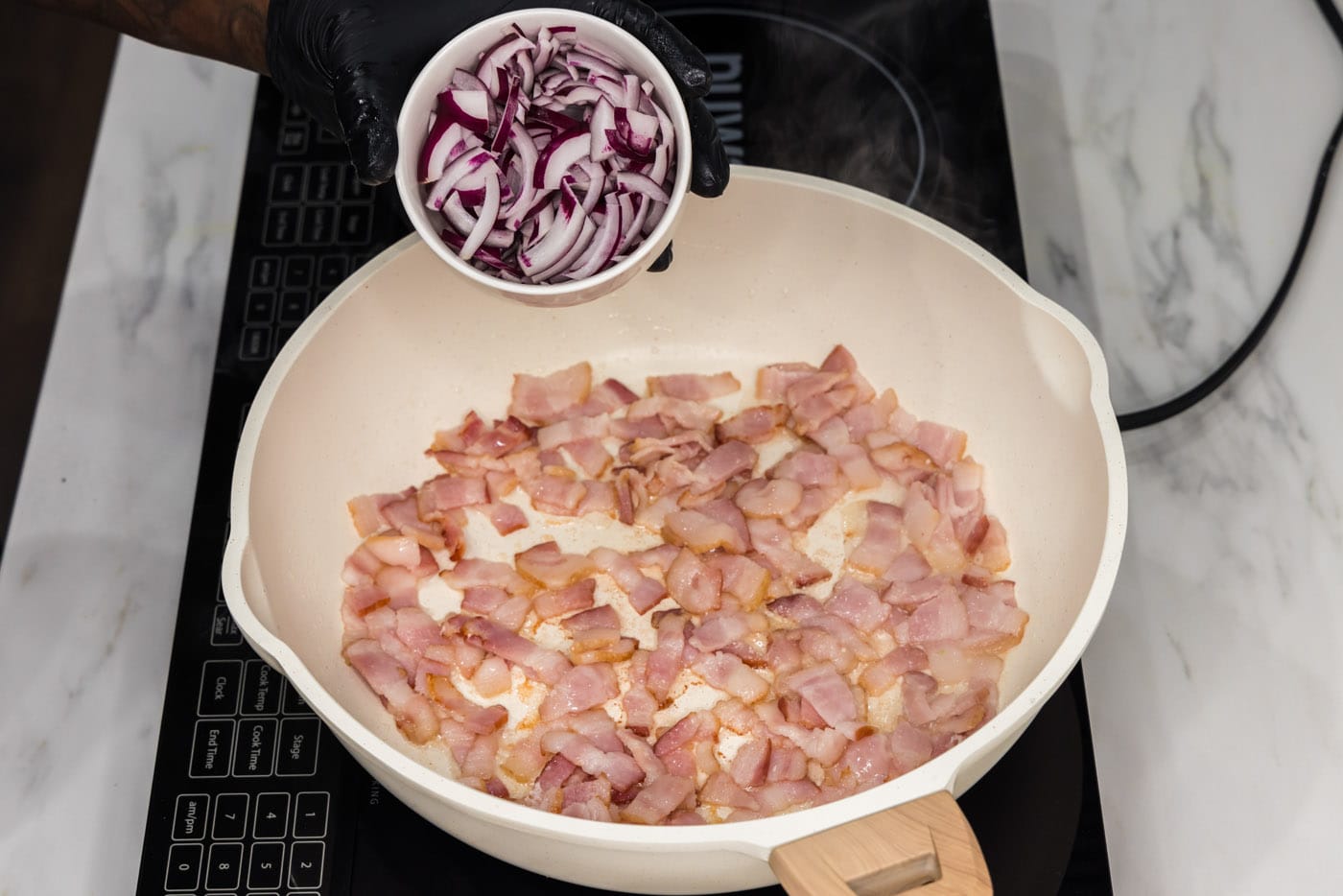adding sliced onion to pan of partially cooked bacon
