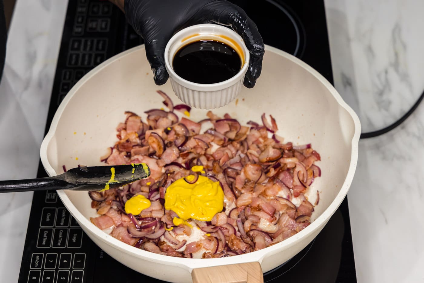 adding soy sauce to skillet with bacon, mustard, and onions