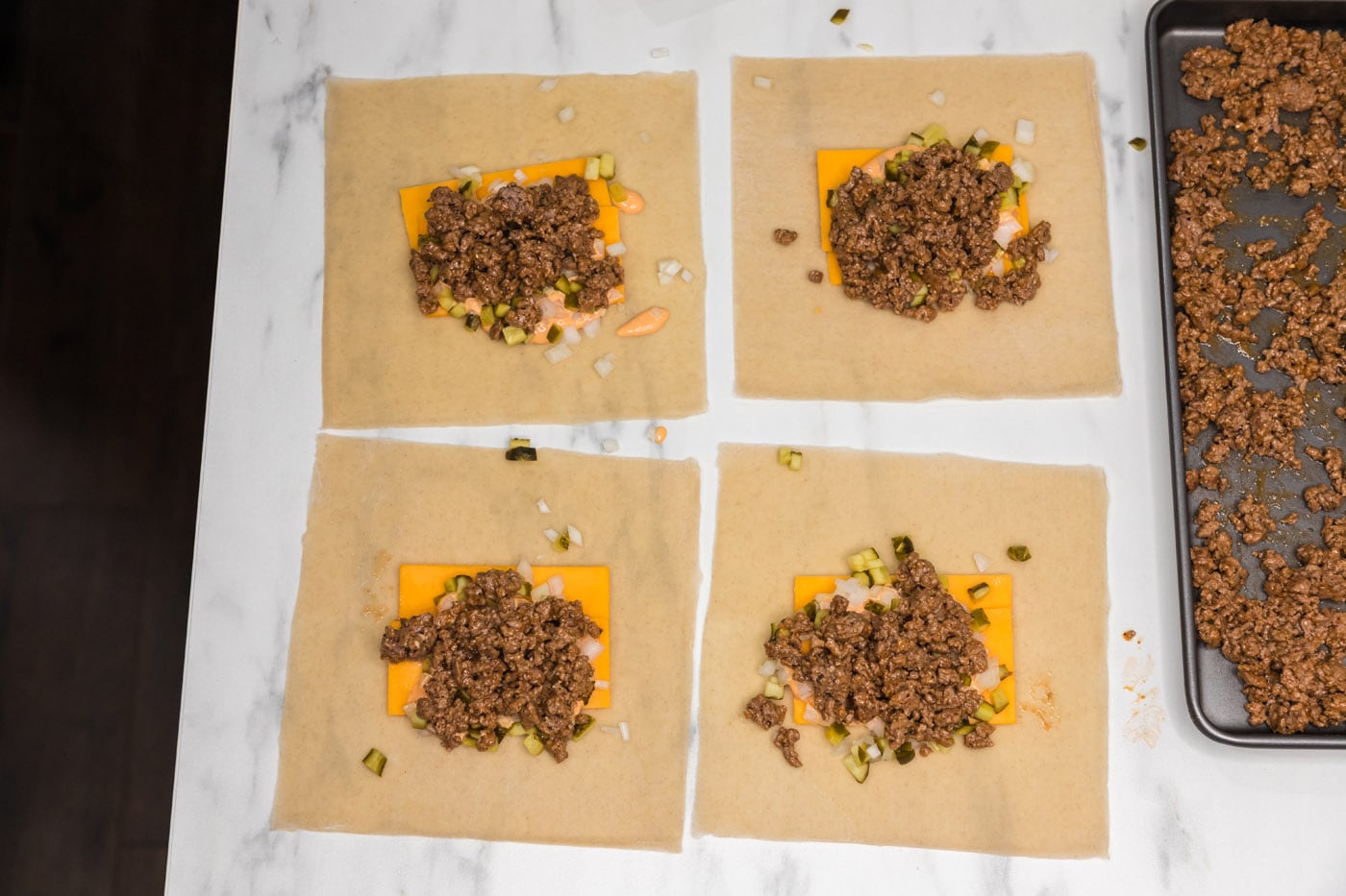 ground beef on top of egg roll wrappers with cheddar cheese, onion, and pickles