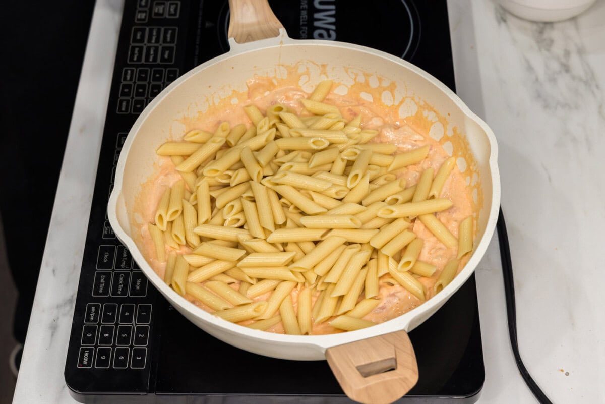 adding pasta to skillet with creamy buffalo sauce
