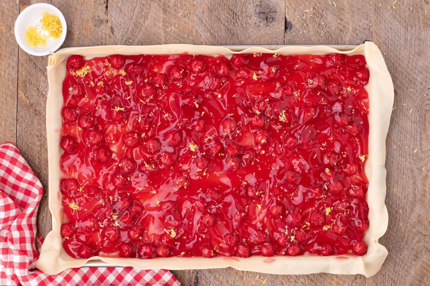 cherry pie filling on top of pie crust in a jelly roll pan