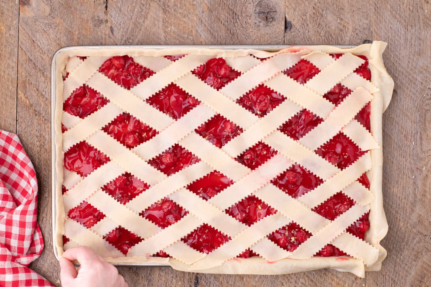 pinching seams of pie crust together to seal edges of cherry slab pie