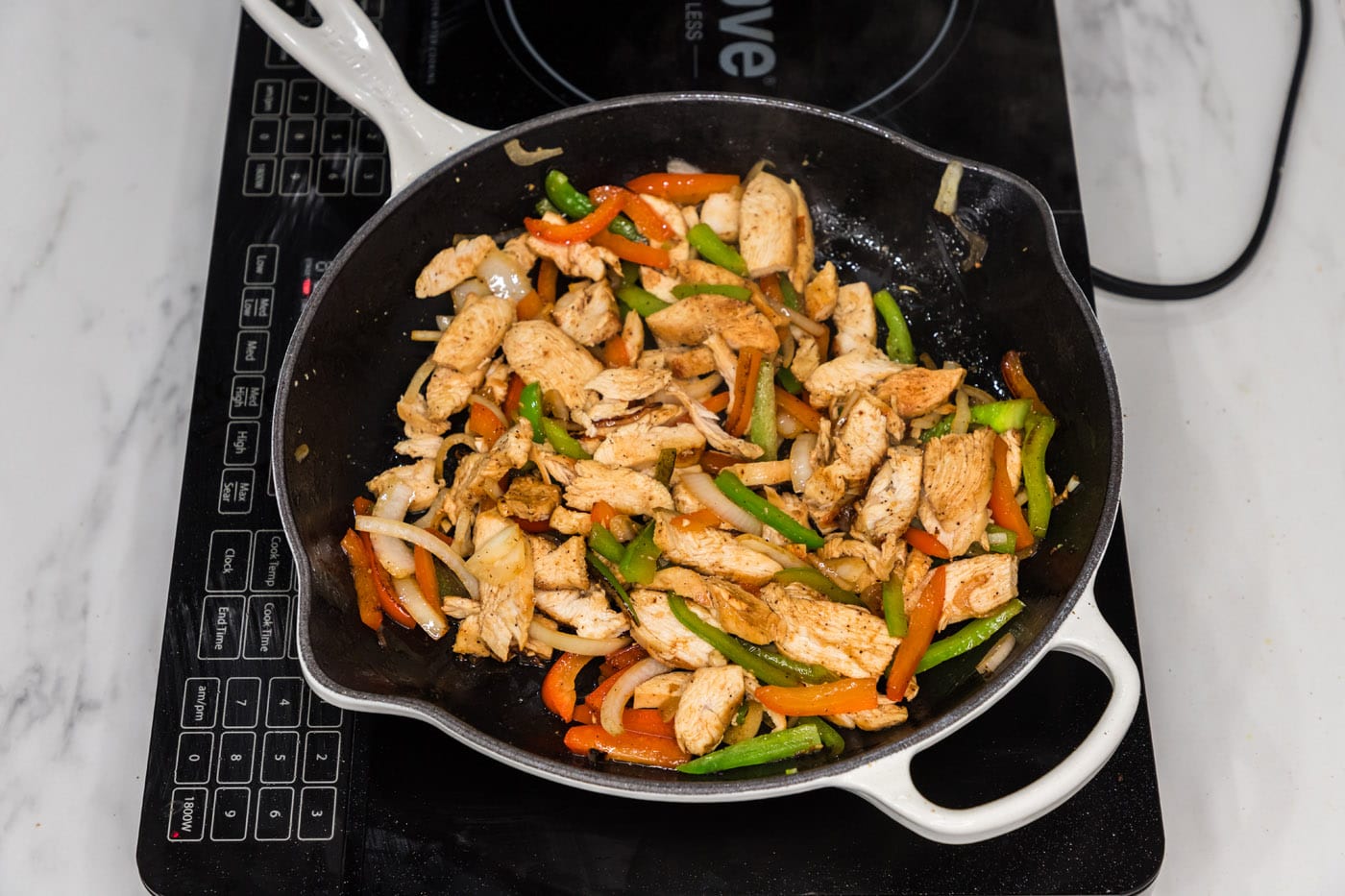 sliced chicken added to skillet with bell peppers and onion