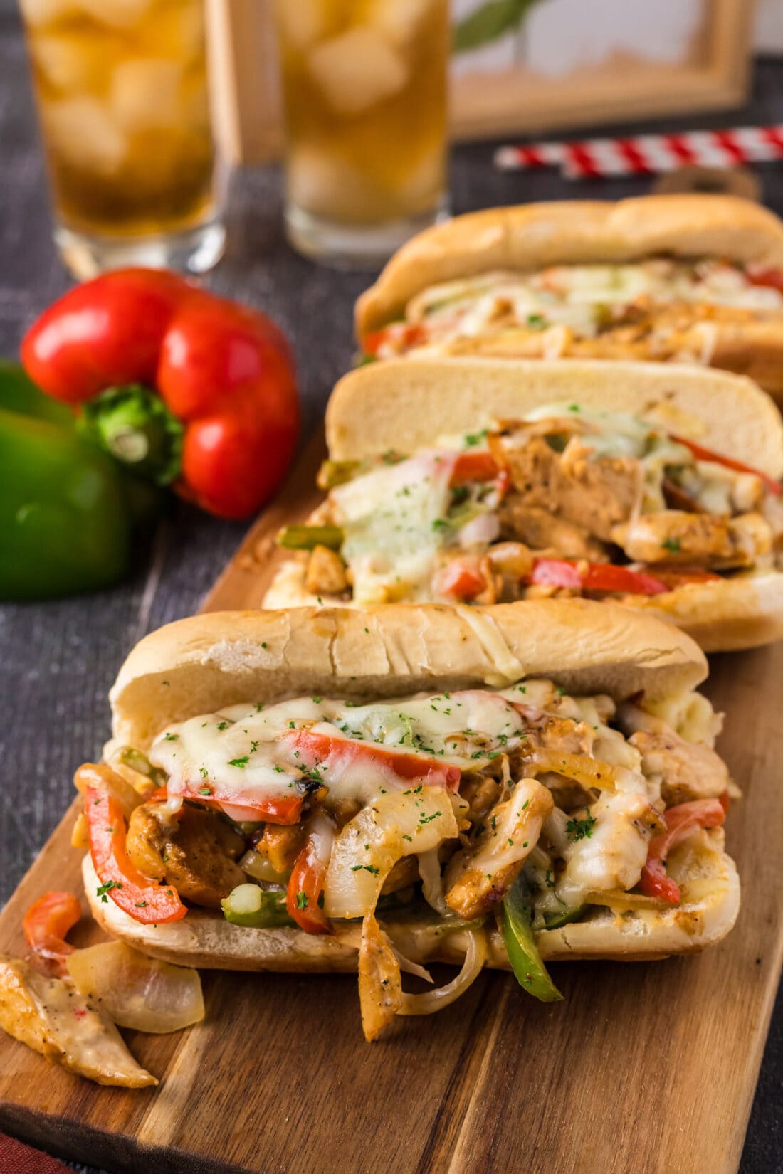 Three Chicken Philly Cheesesteaks on a wooden serving board