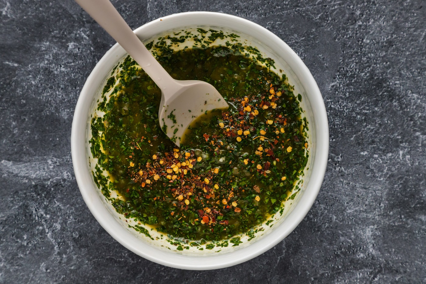 chimichurri sauce in a mixing bowl with red pepper flakes