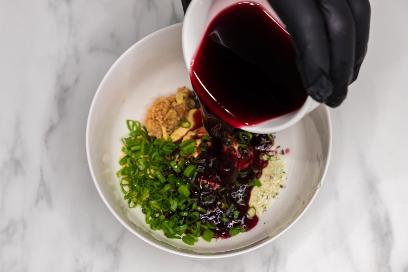 pouring red wine over garlic, rosemary, chili powder, mustard powder, Dijon mustard, and green onion