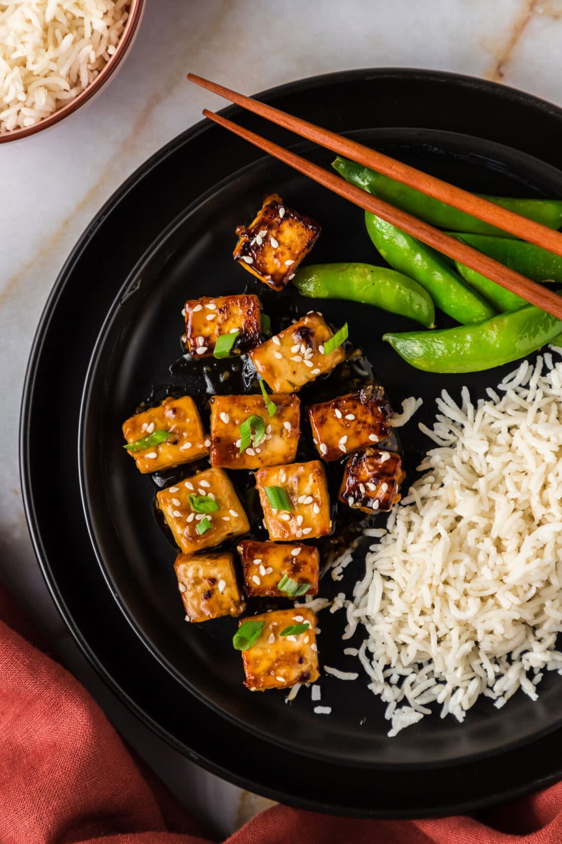 Close up photo of Honey Garlic Tofu on a plate with rice and snap peas