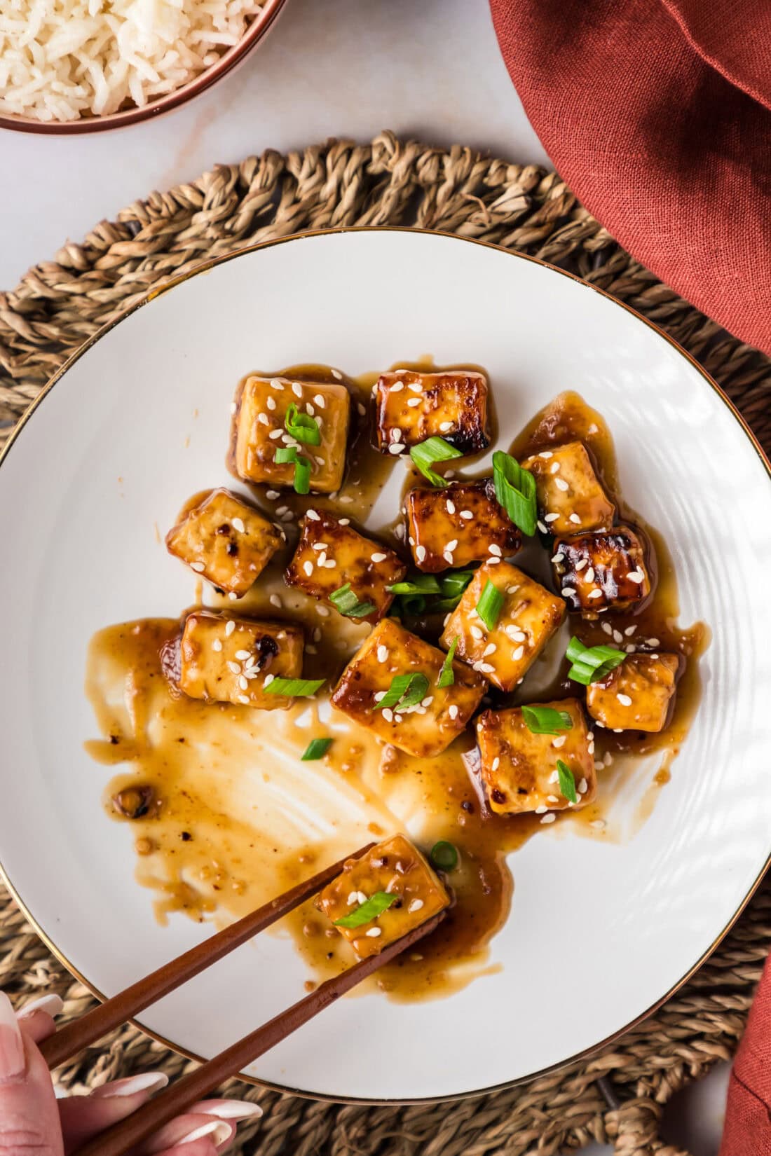 Chopsticks grabbing a piece of Honey Garlic Tofu on a plate 