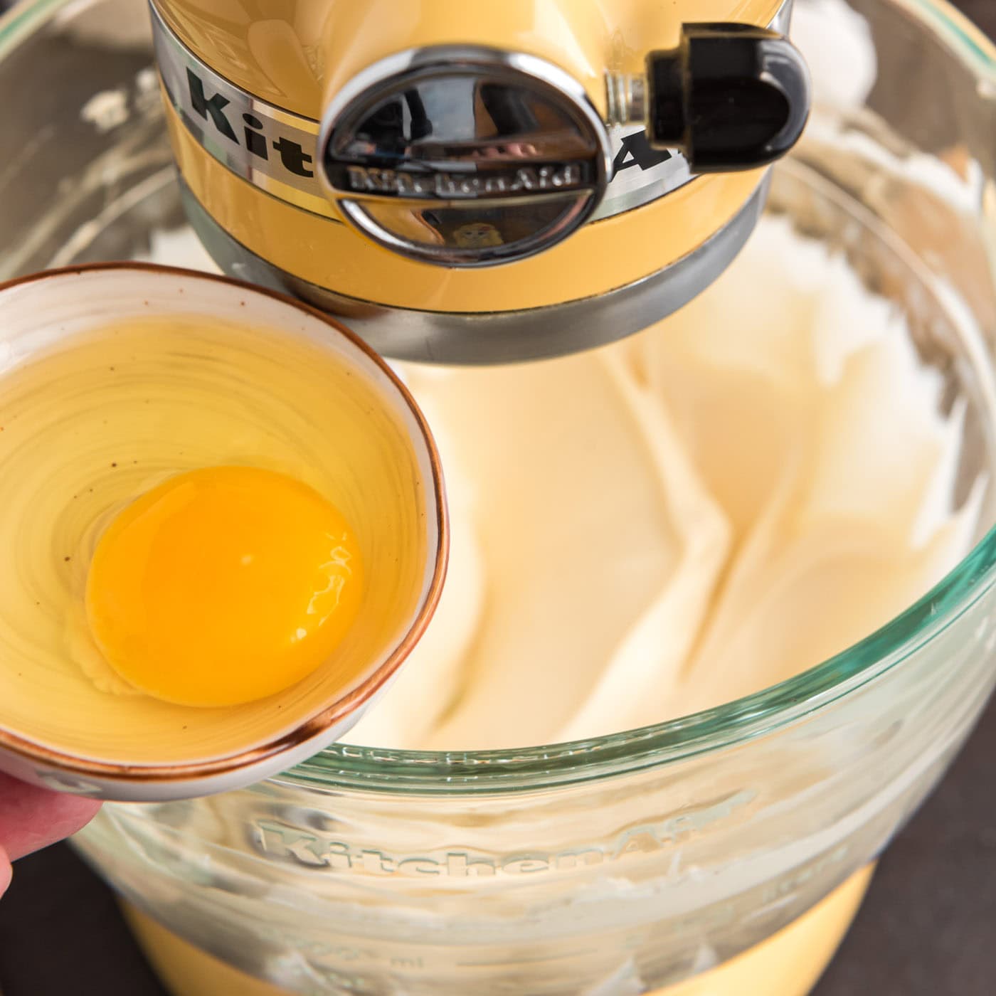 adding egg to stand mixer bowl with cheesecake filling