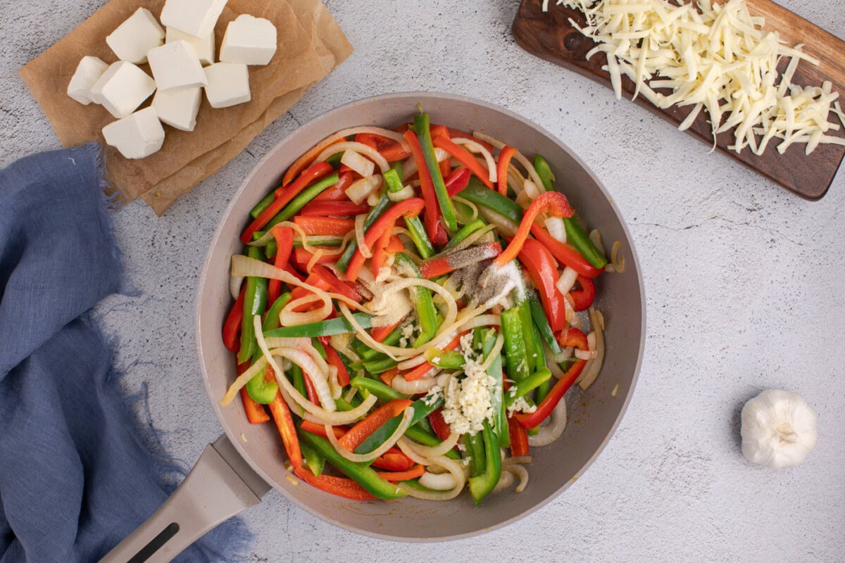 seasonings and garlic added to skillet with sauteed peppers and onions