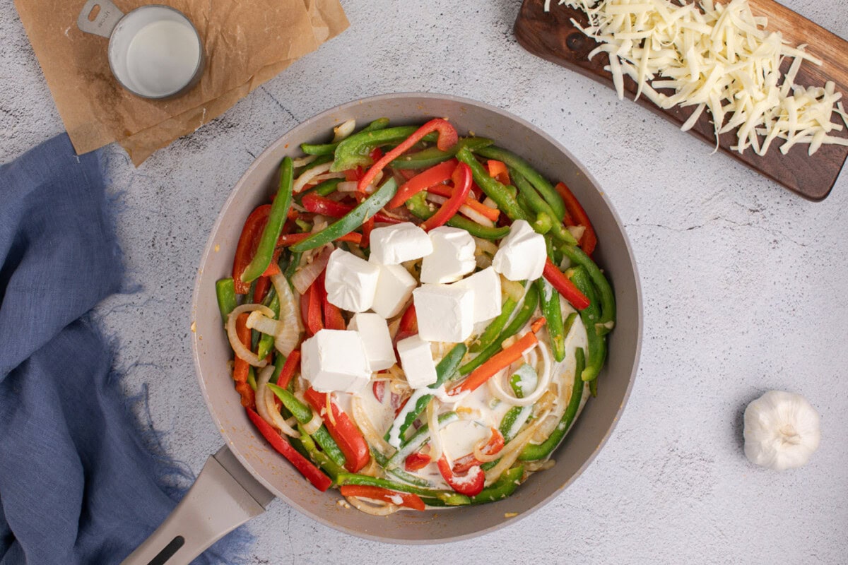 cubed cream cheese on top of sauteed peppers and onions in a skillet