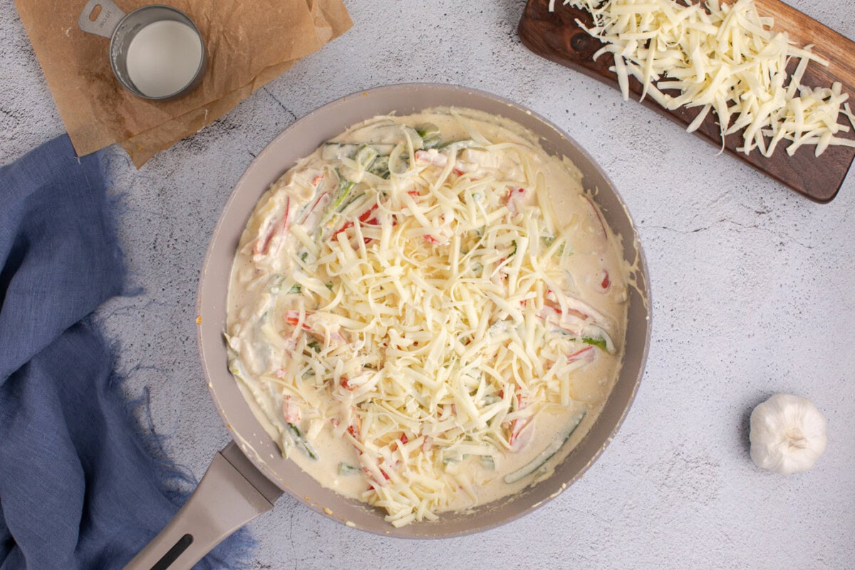 adding pepperjack cheese to skillet with sauteed peppers and onions