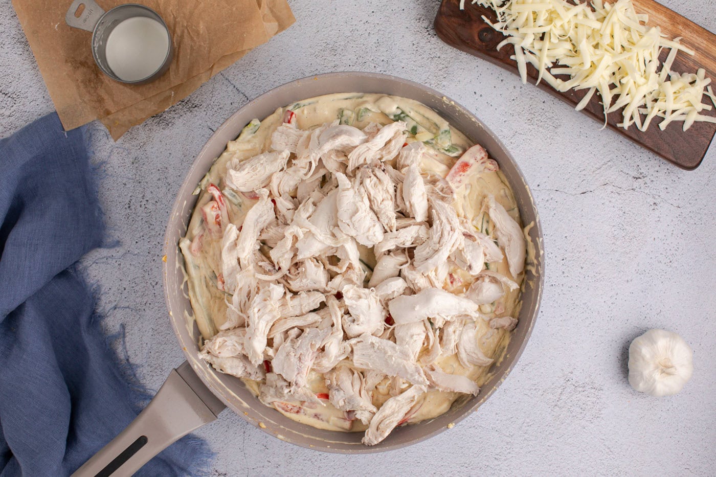 shredded chicken in skillet with creamy sauce, peppers, and onions