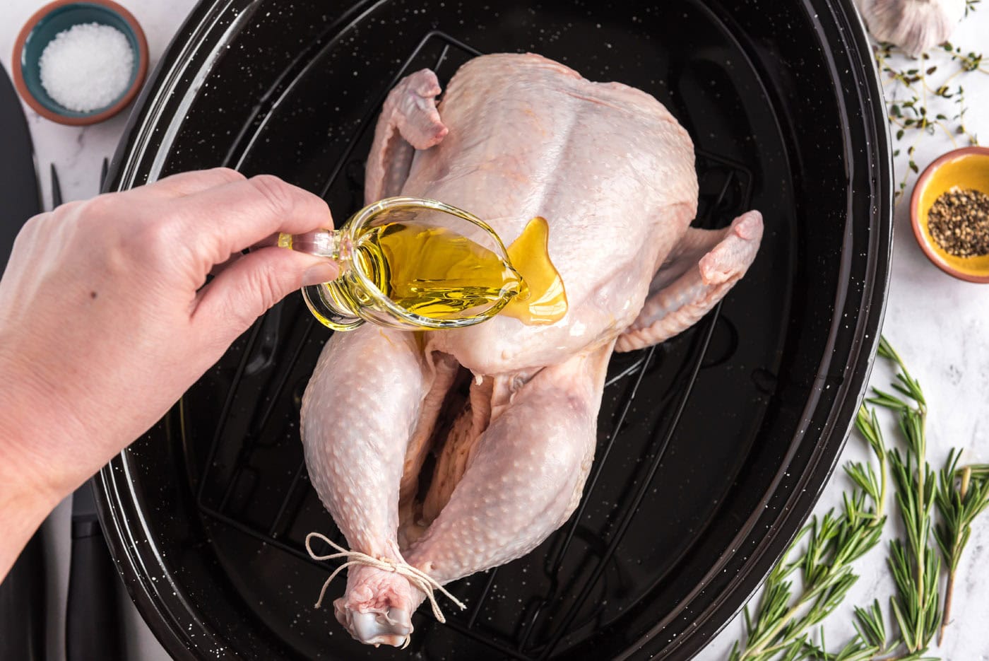 pouring olive oil over raw chicken in a roasting pan