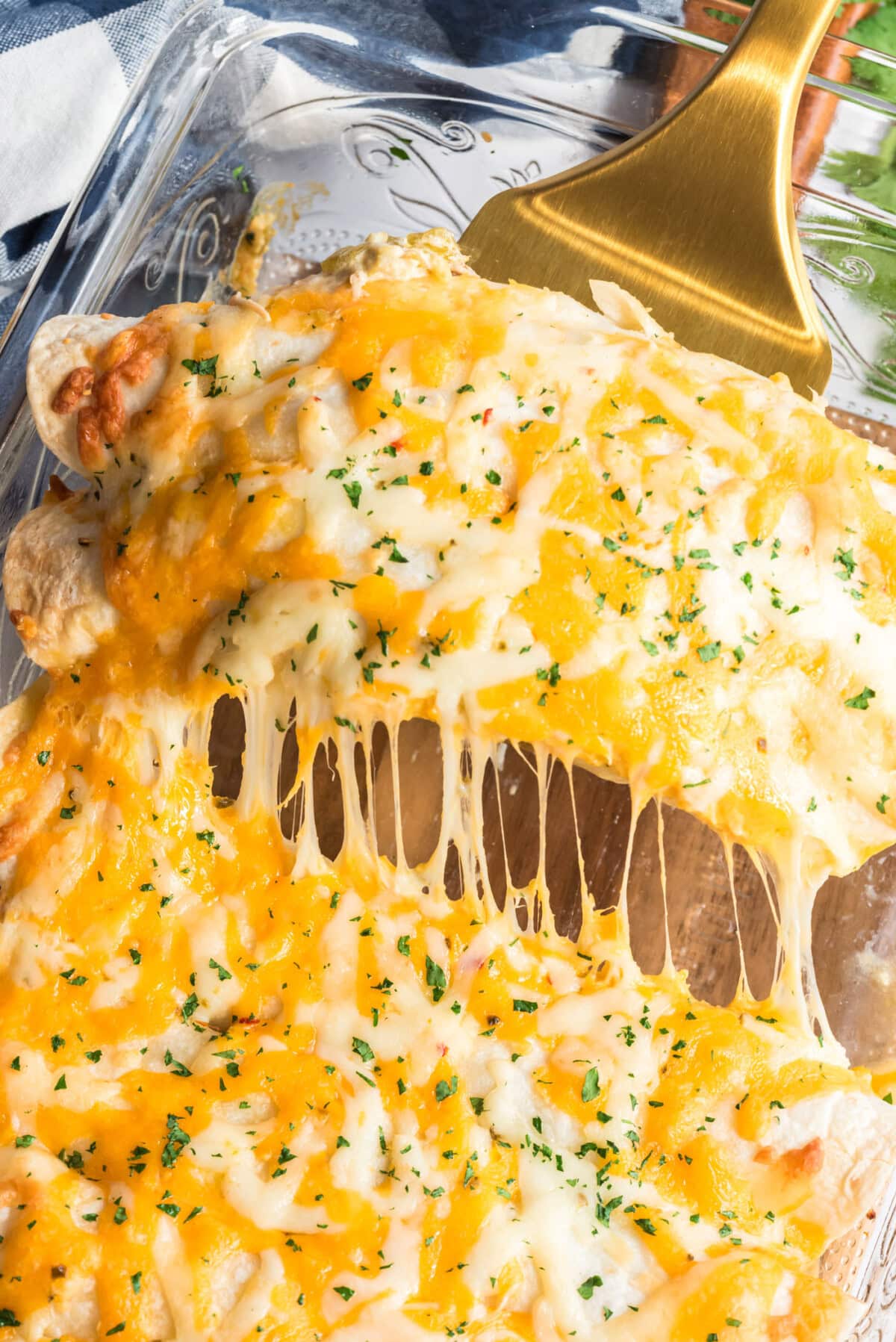 Spatula pulling up two Shredded Chicken and Chile Enchiladas from the pan