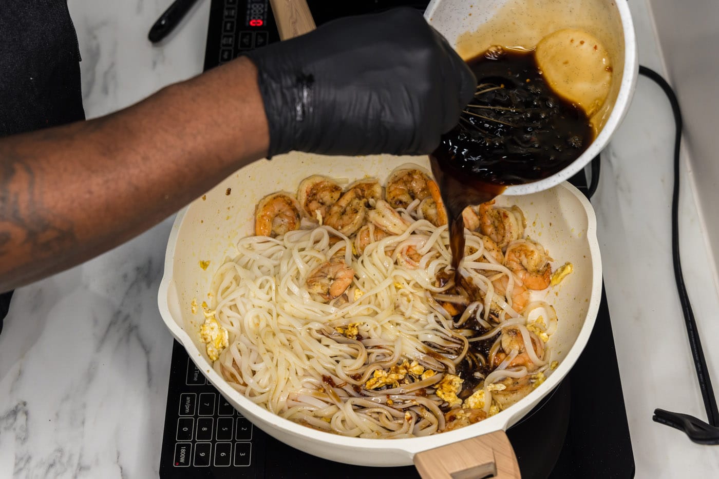 pouring pad thai sauce into skillet with rice noodles and shrimp