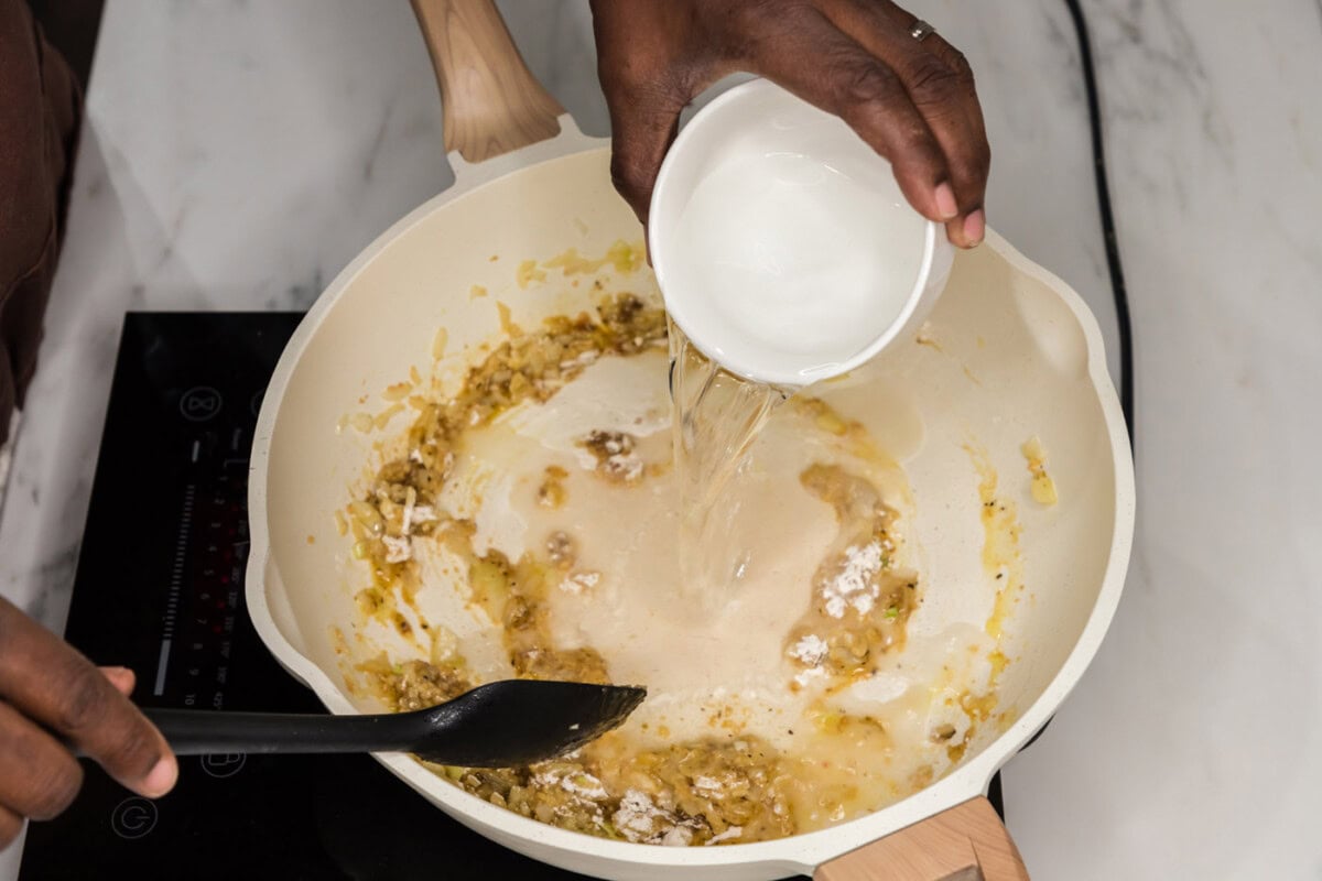 mixing water into skillet with bouillon base, onion, flour, and garlic