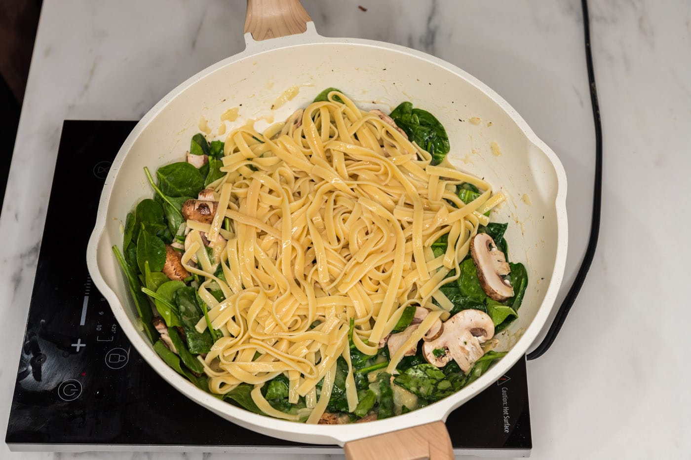 fettuccine noodles added to spinach and mushroom mixture in a skillet