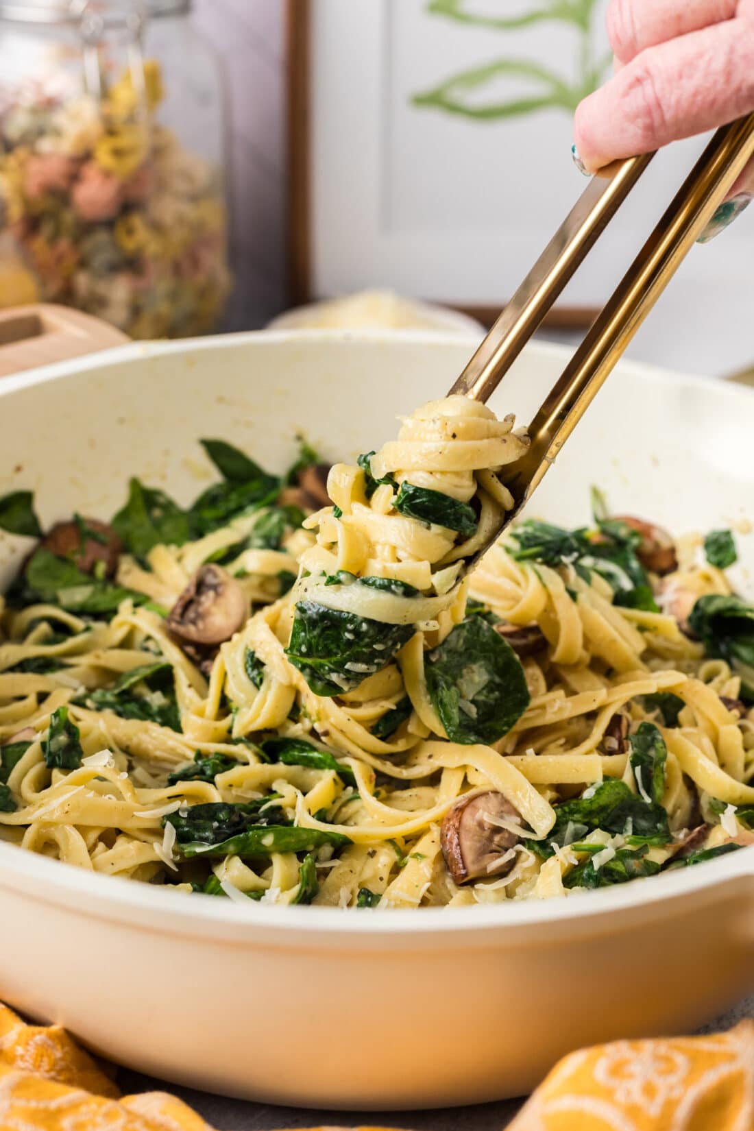 Spinach Fettuccine wrapped around a pair of tongs being lifted out of a skillet