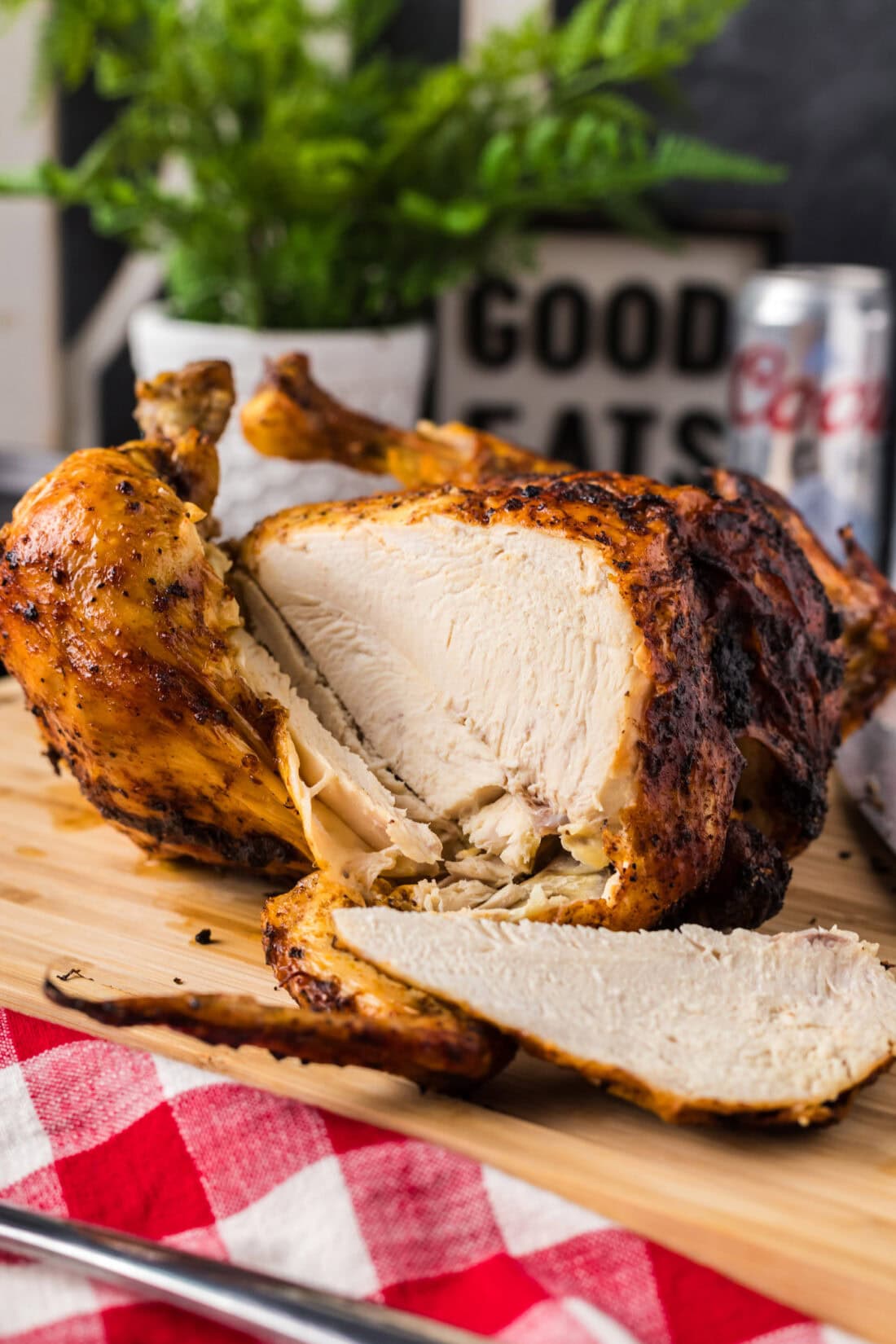 Slice of Beer Can Chicken resting on a wooden cutting board with the rest of the Beer Can Chicken behind it