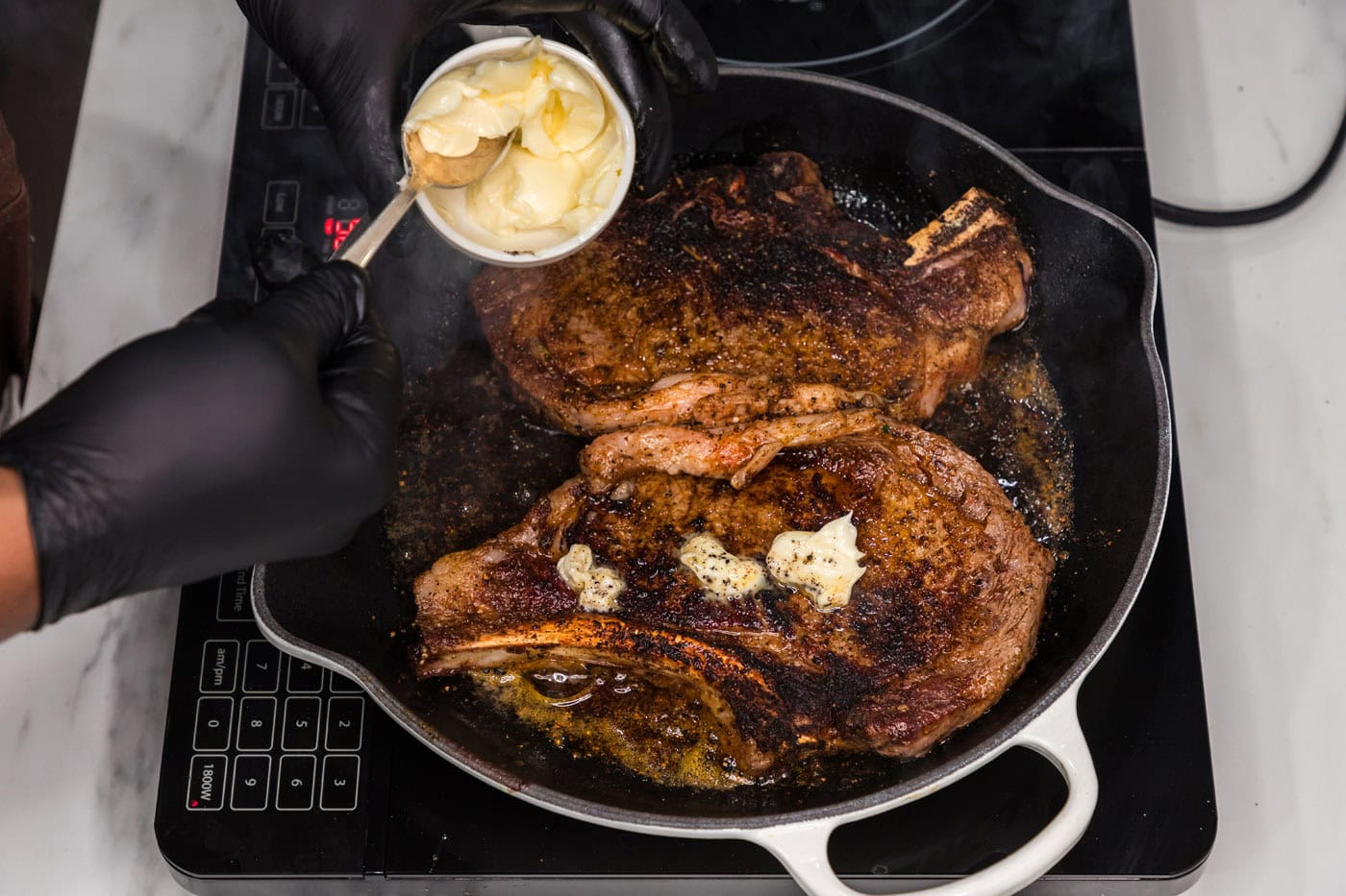 adding butter on top of ribeye steaks in a skillet