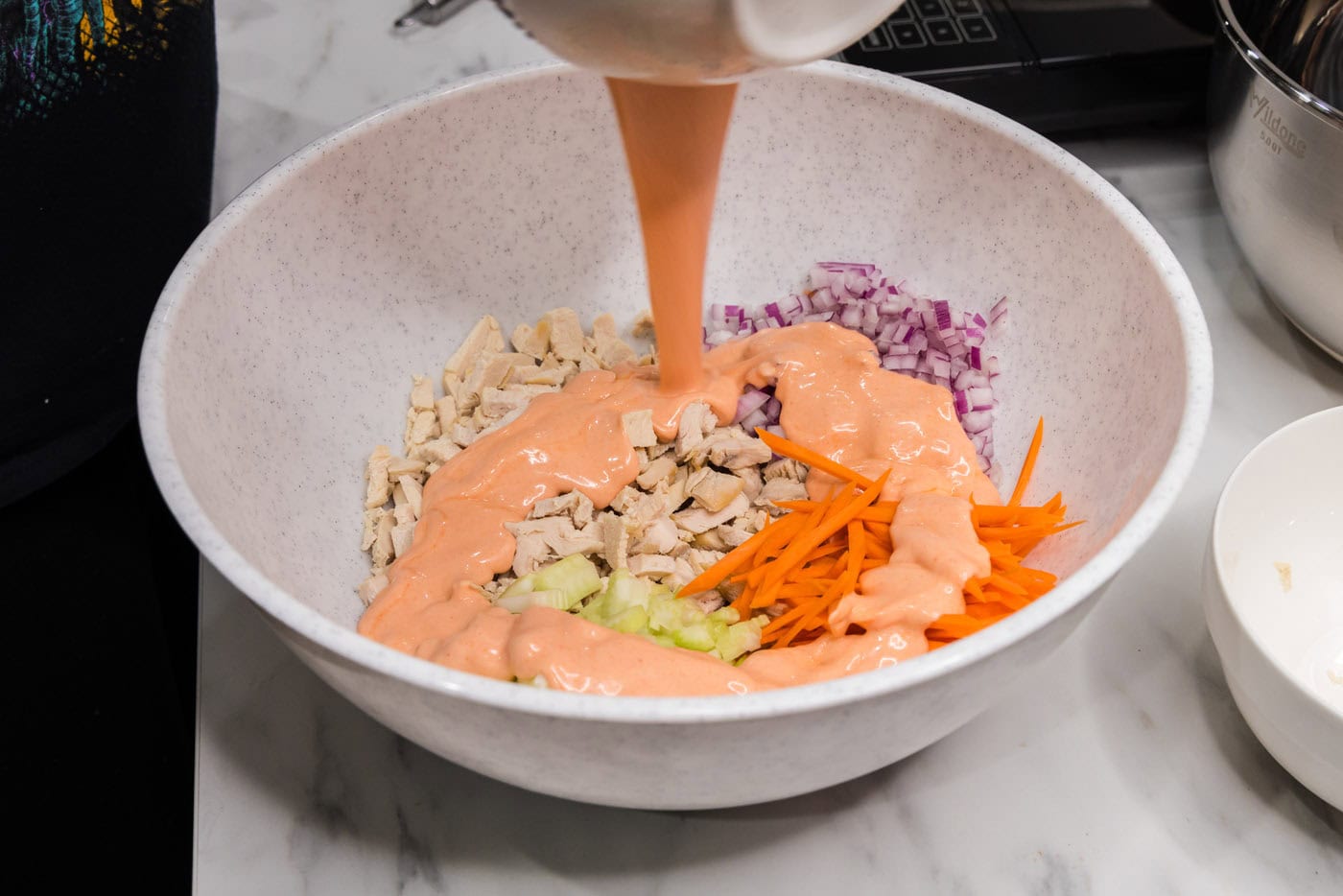 pouring buffalo sauce over chicken and vegetables in a bowl