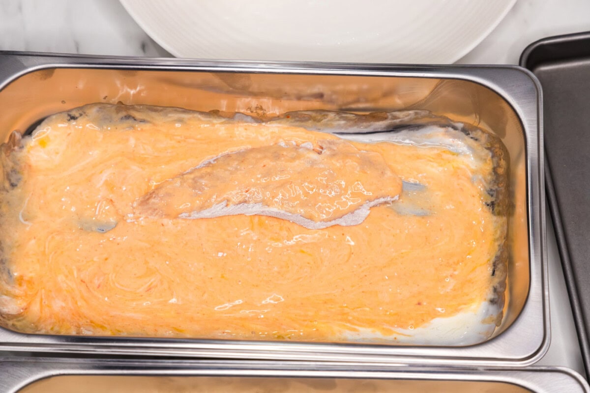 adding flour dredged chicken to pan of buttermilk and hot sauce mixture