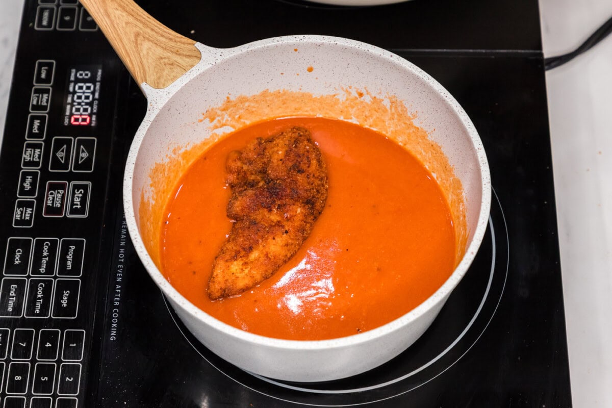fried chicken tender dipped into buffalo sauce in a pan