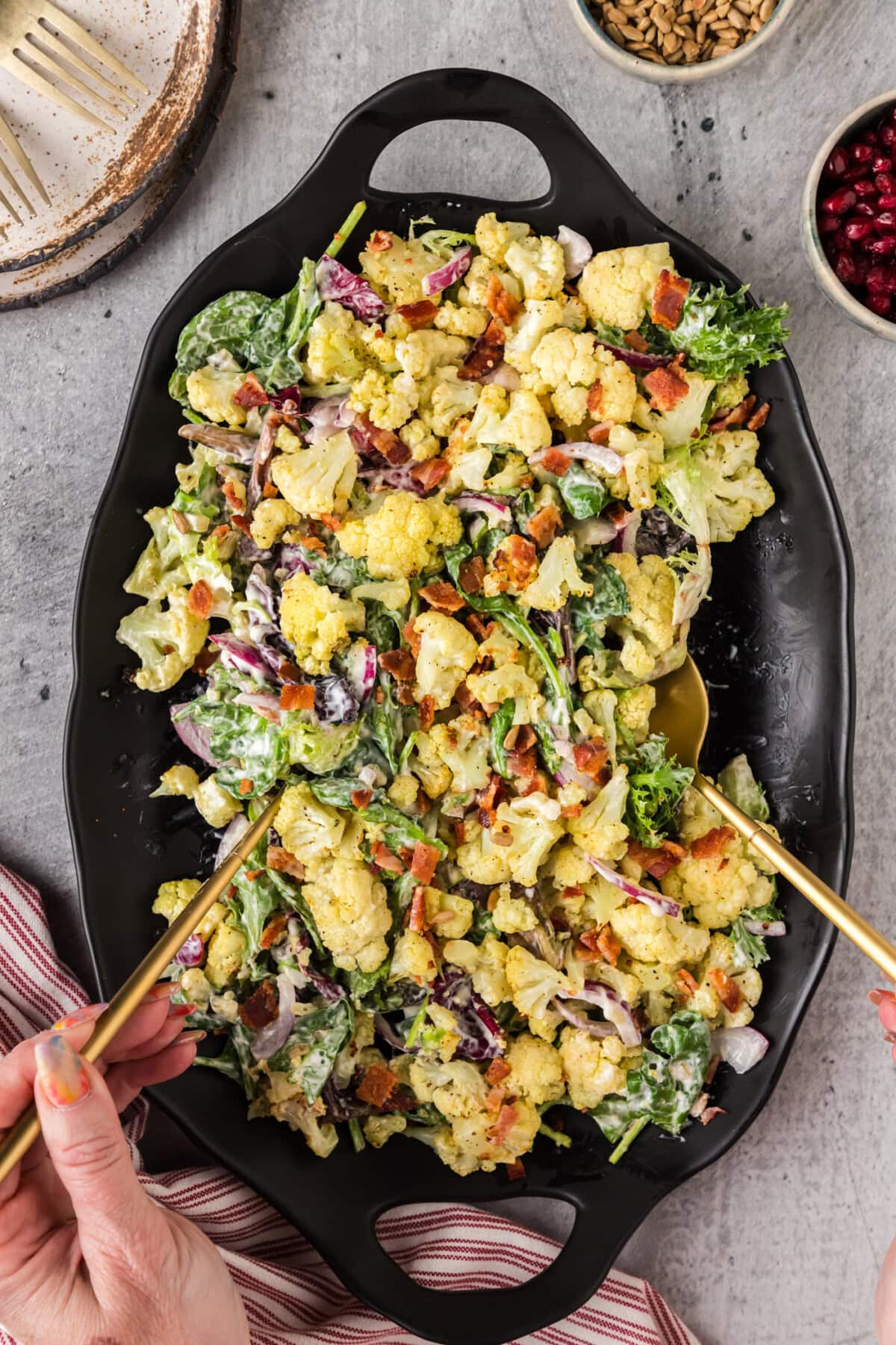 Hands picking up Cauliflower Salad using serving spoons