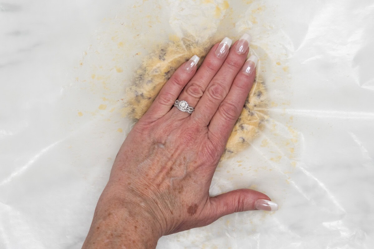hand flattening cookie dough ball with wax paper