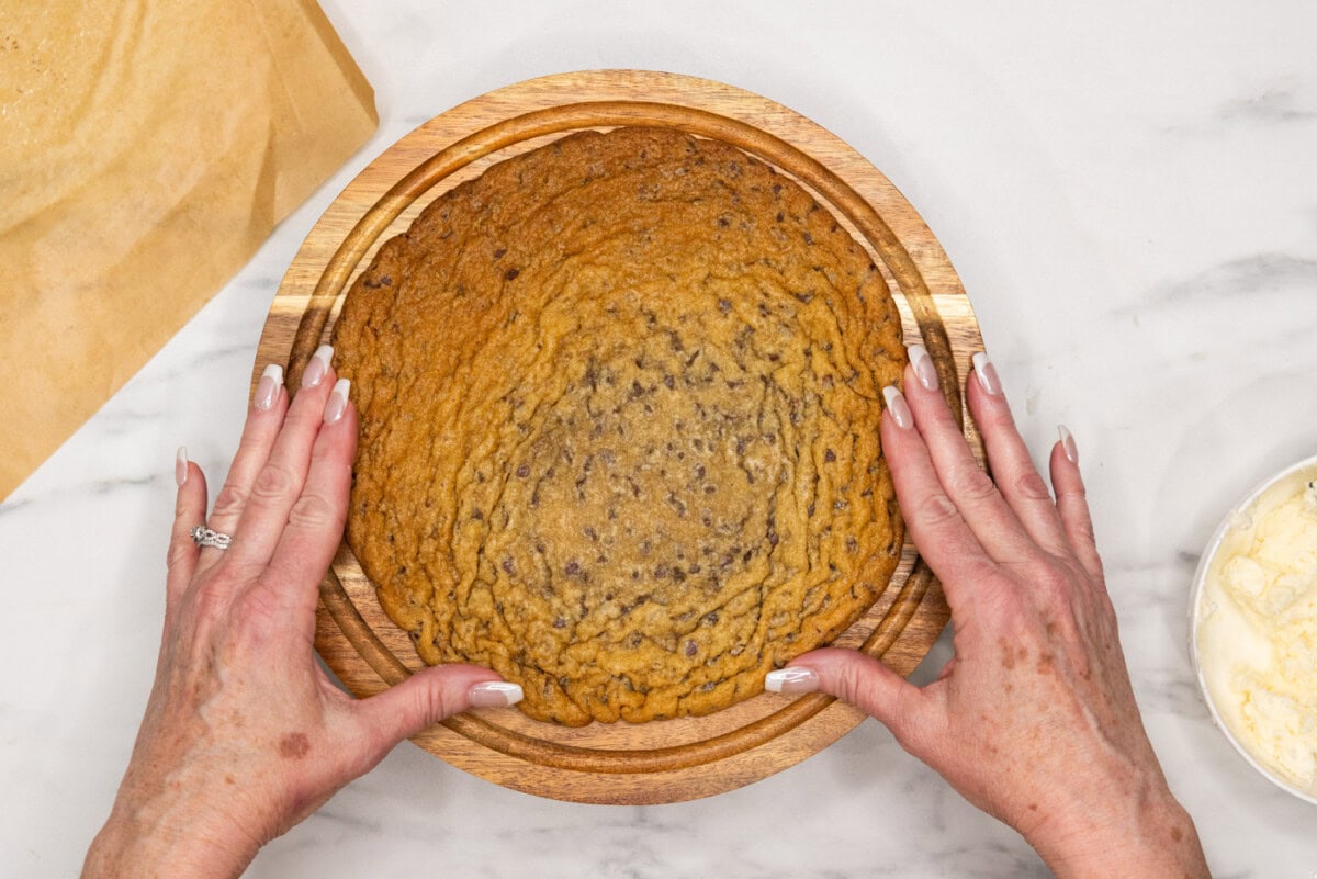 placing jumbo chocolate chip cookie onto cake stand