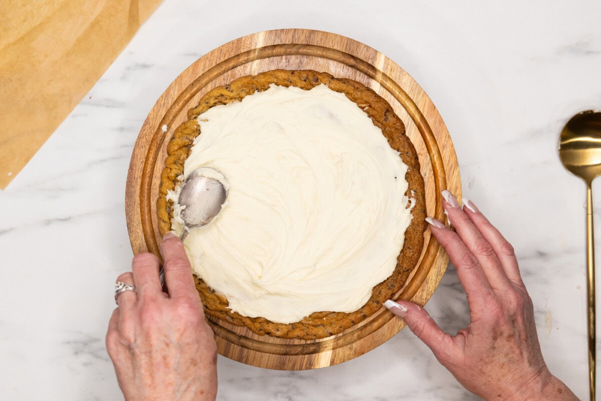 spreading buttercream frosting overtop a jumbo chocolate chip cookie