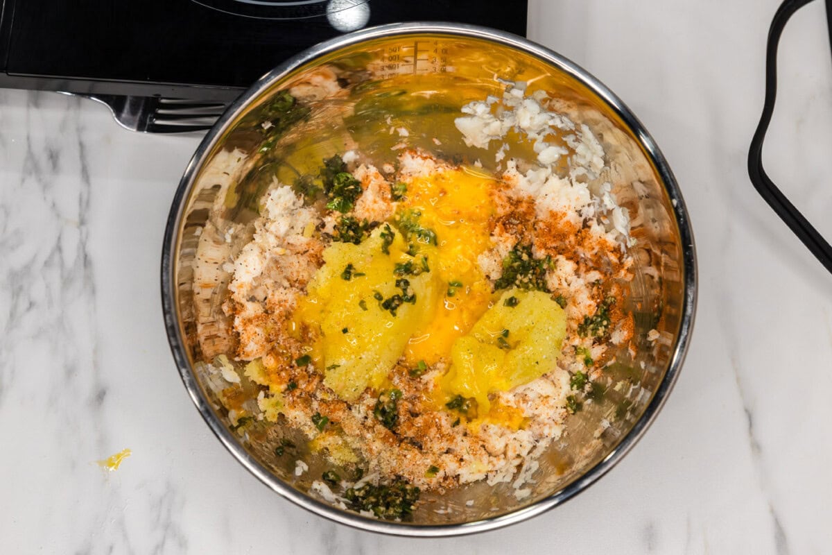 flaked fish with seasonings, egg, and mashed potatoes in a bowl