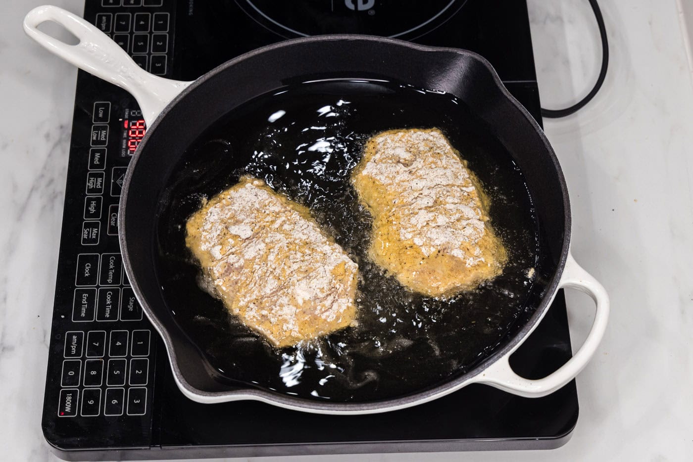 frying chicken burgers over hot oil in a skillet