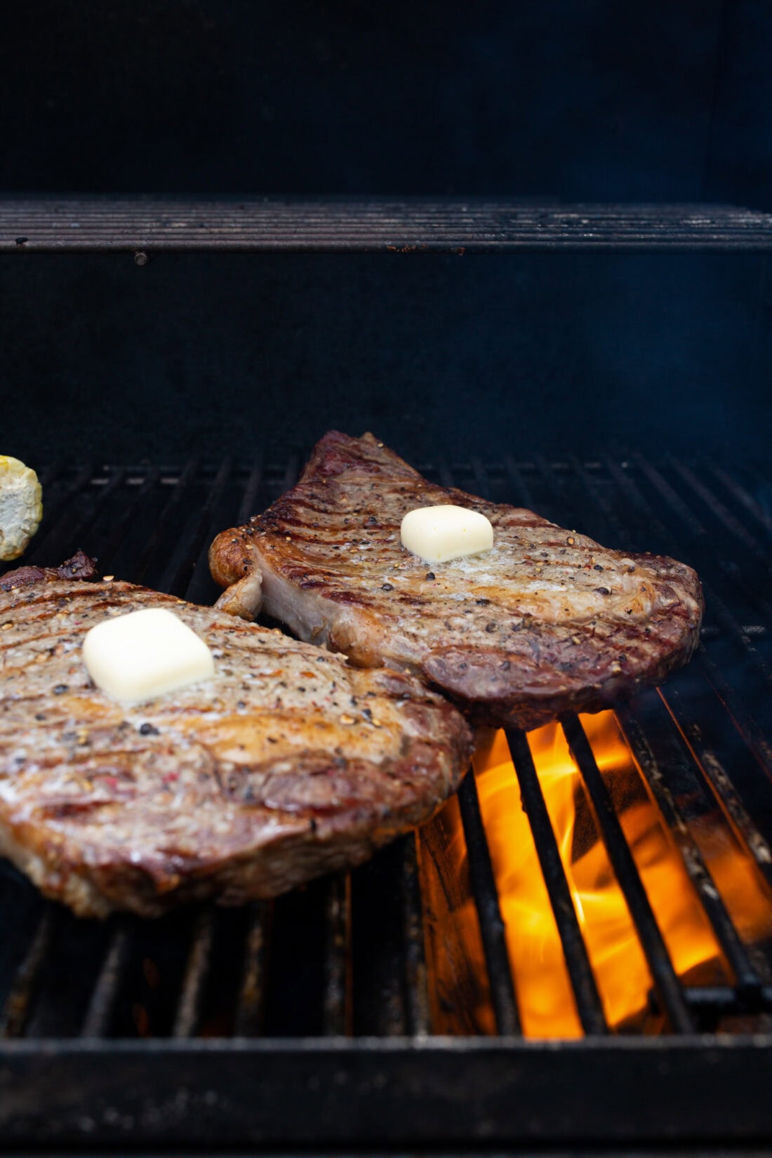 Two steaks on the grill with pats of butter