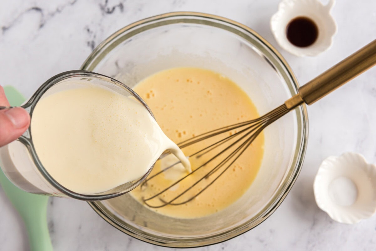 pouring heavy cream into bowl of whisked eggs and sugar mixture