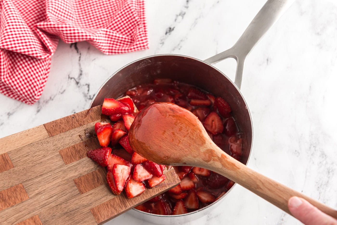 adding a quart of strawberries to homemade strawberry sauce in a saucepan