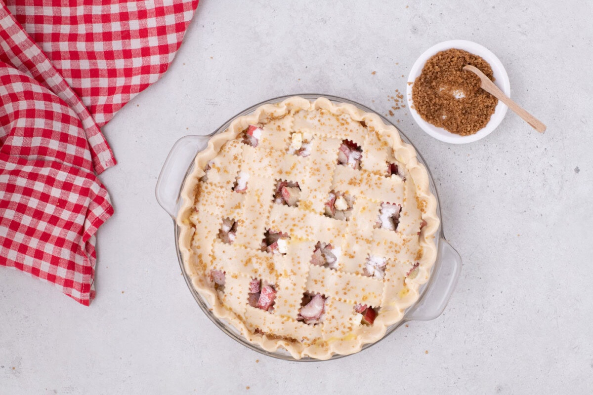sprinkling turbinado sugar over lattice top rhubarb pie
