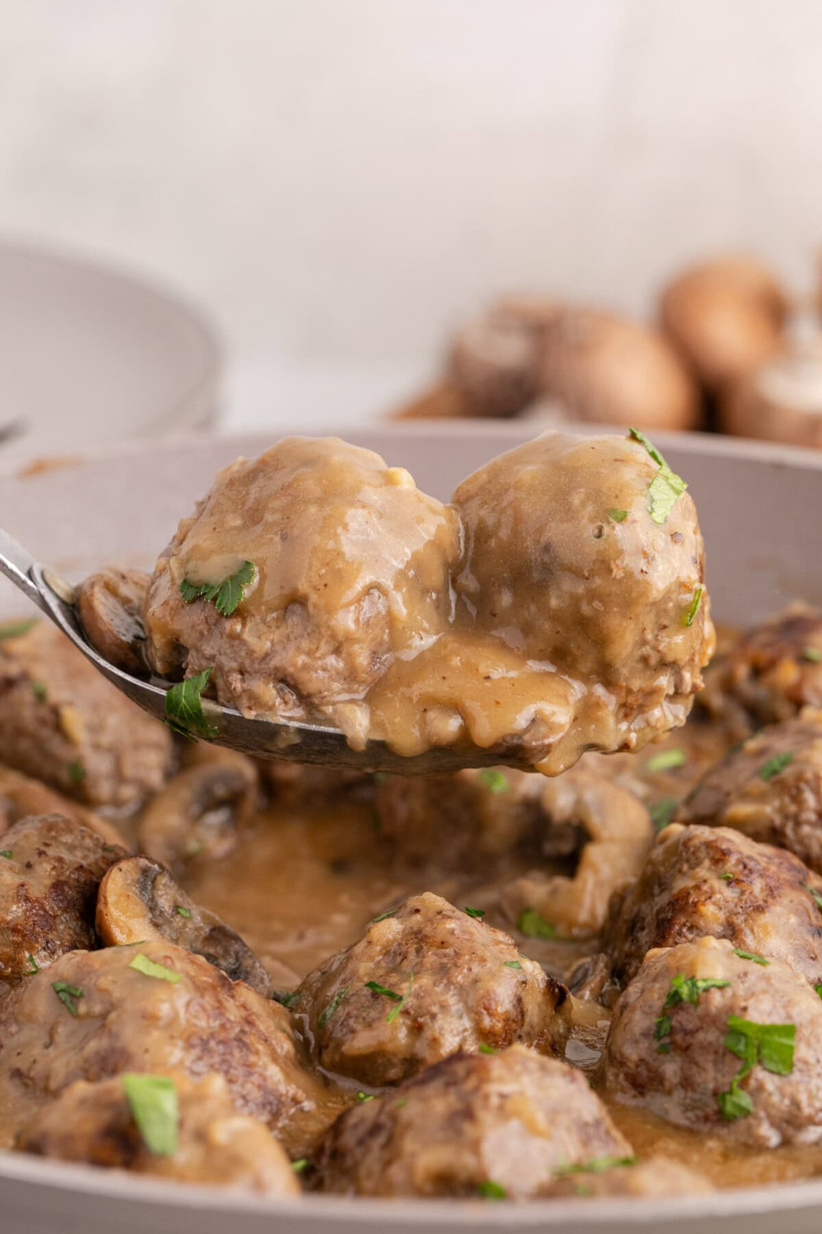 Two Salisbury Steak Meatballs on a spoon held above a skillet of Salisbury Steak Meatballs