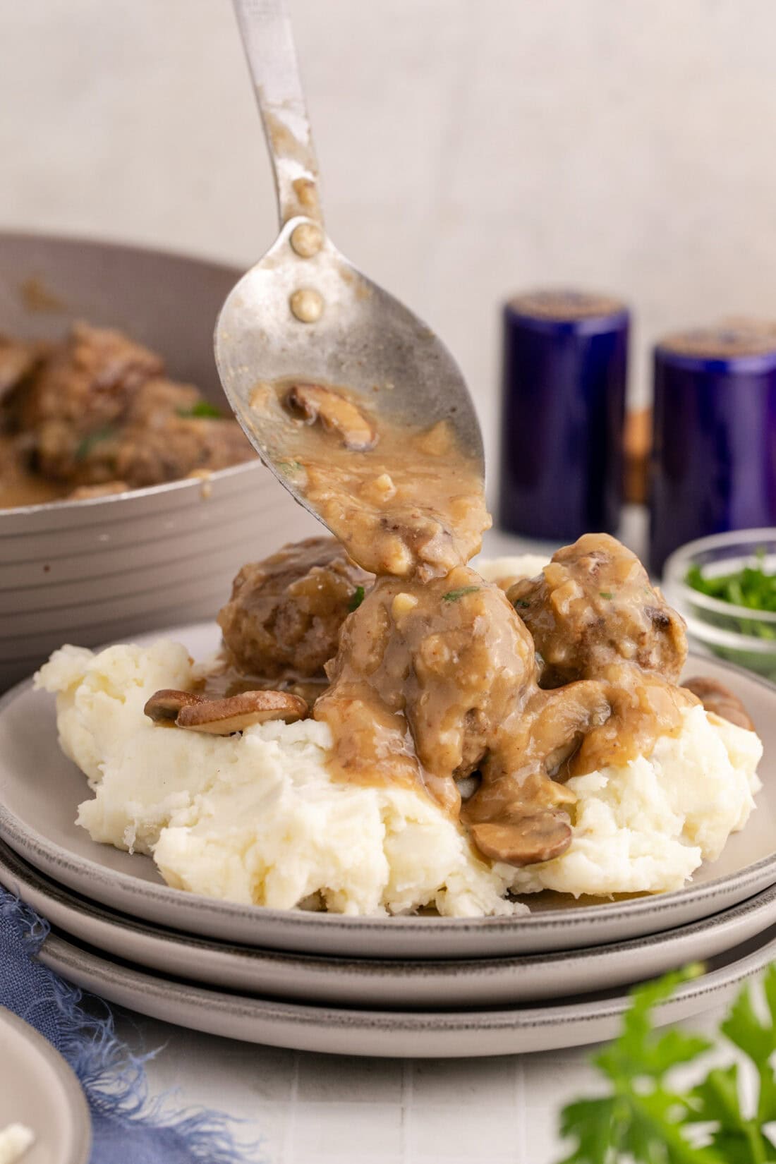 Gravy being spooned over Salisbury Steak Meatballs and mashed potatoes
