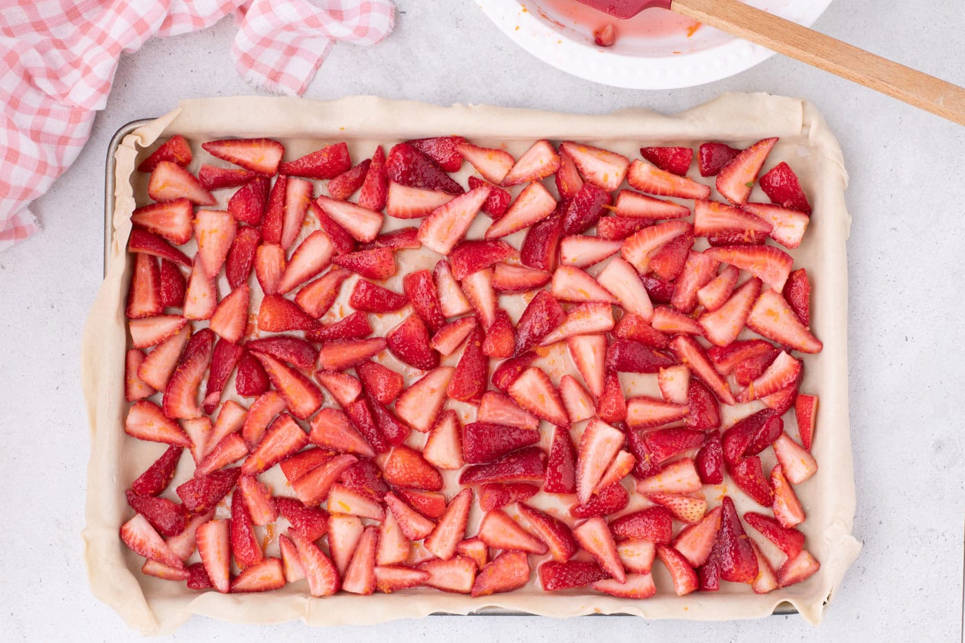 sliced strawberries on top of pie crust in a jelly roll pan