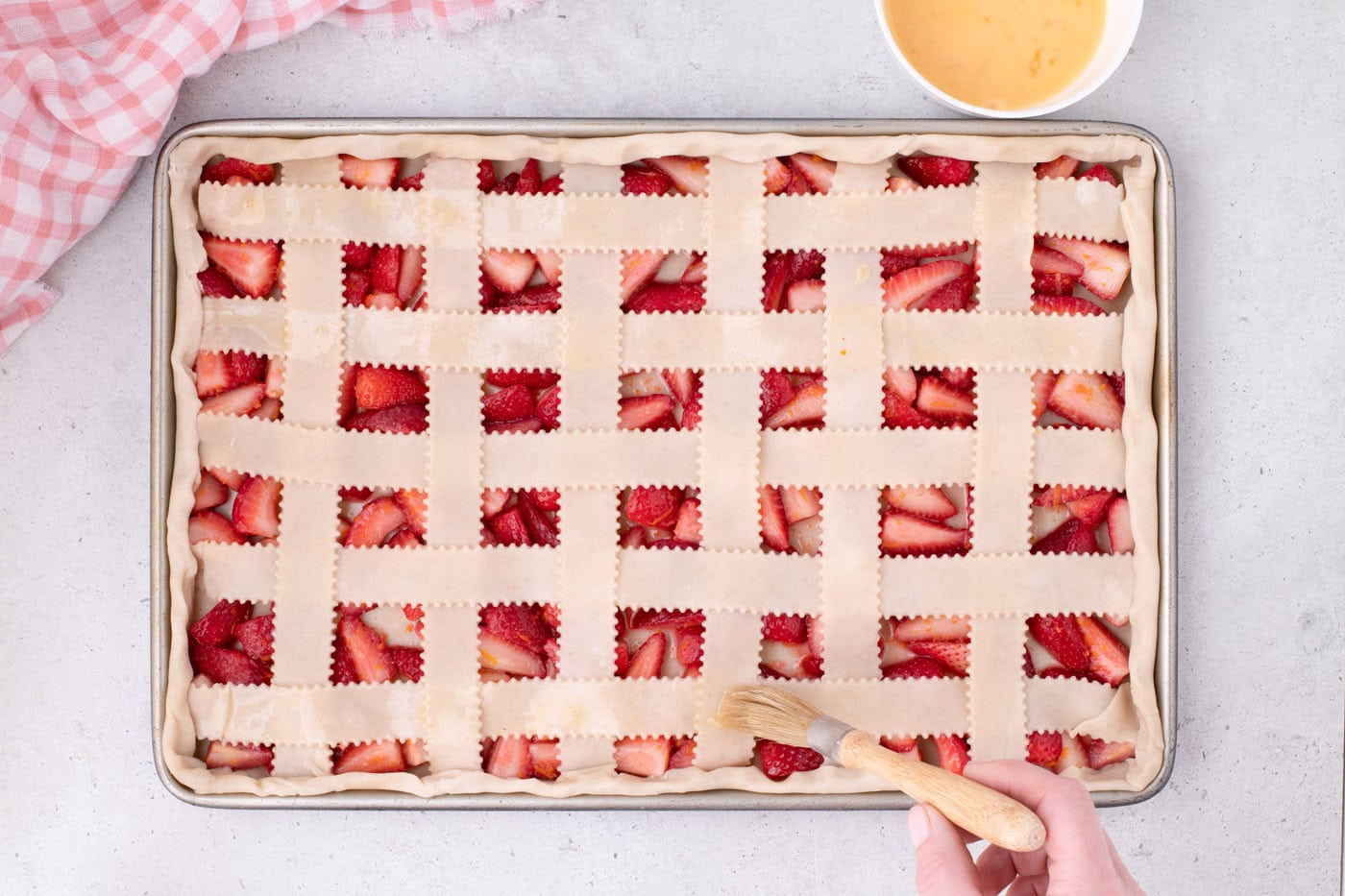 brushing strawberry slab pie with egg wash