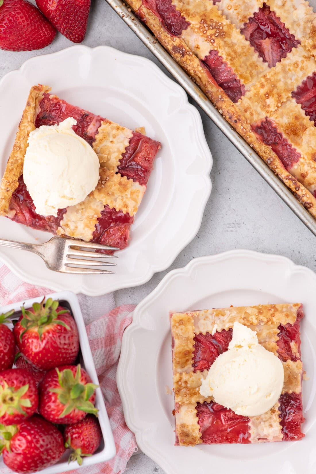 Two sliced of Strawberry Slab Pie on plates topped with ice cream