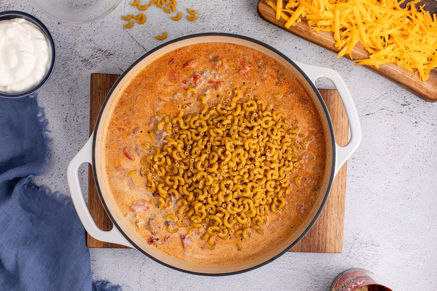 adding noodles to taco macaroni and cheese in a skillet