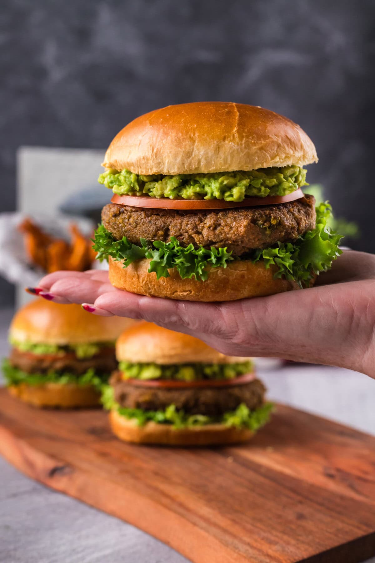 Hand holding up a Veggie Burger with two more on a platter in the background