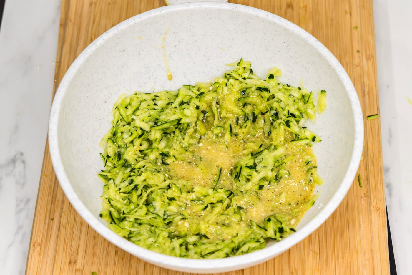 egg added to shredded zucchini in a bowl