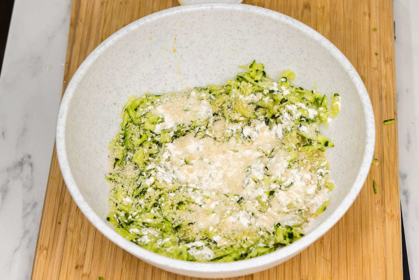 flour and breadcrumbs added to shredded zucchini mixture in a bowl