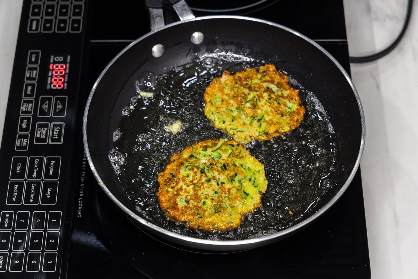fried zucchini fritters in a skillet of oil